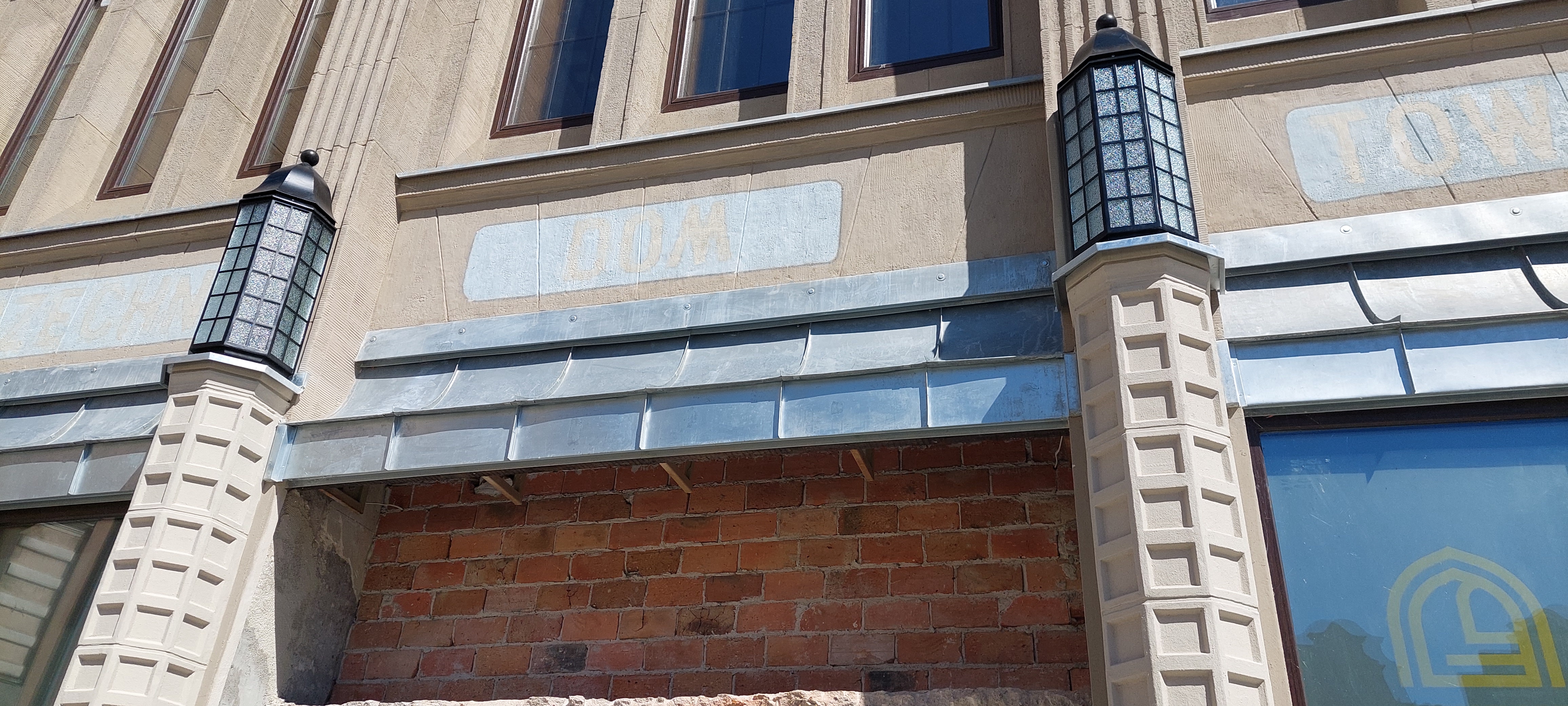 Dwie ozdobne lampy już są umocowane na kolumnach przy wejściu do remontowanego Domu Towarowego Korzeniewskich w Grudziądzu (zdjęcia)